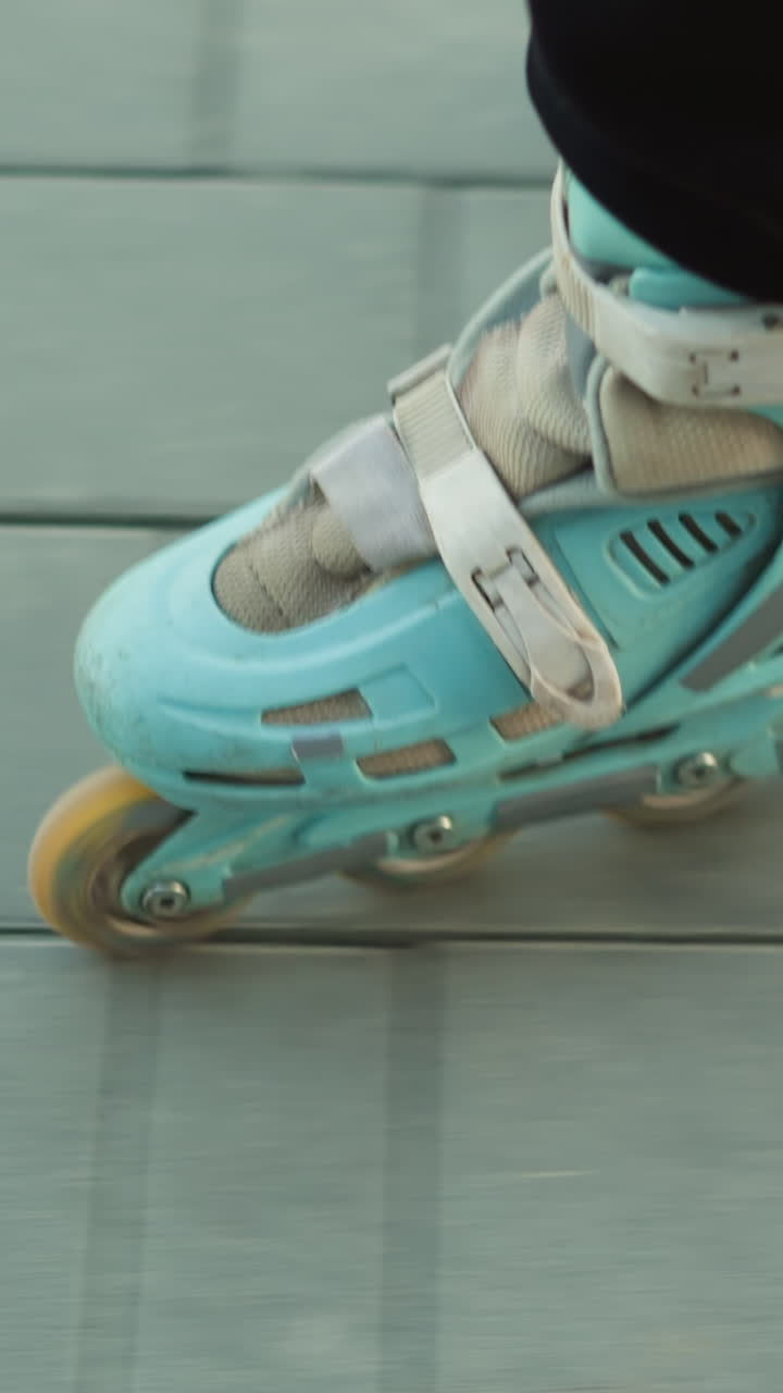 A close-up shot capturing the motion of rollerblades gliding smoothly over a paved path in a park. The person wearing the rollerblades is dressed in black trousers, emphasizing the fluid movement