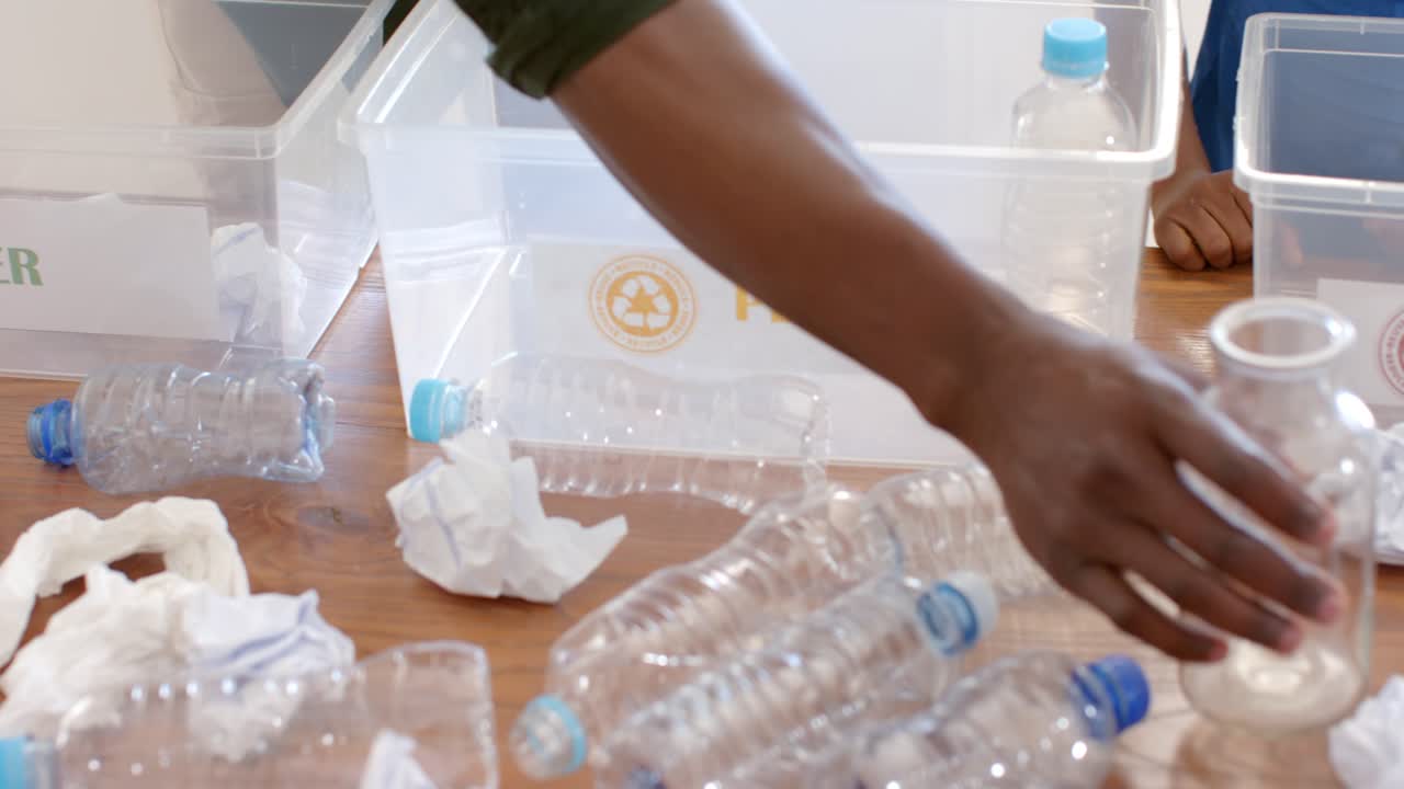 Child reaching is placing paper into PAPER bin, adult is picking PLASTIC bottle and guiding sorting