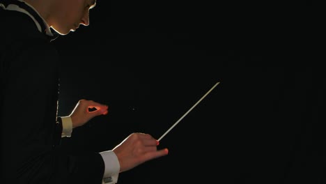 symphony orchestra conductor wearing suit is directing musicians with movement of baton on black background with lights. conducting, directing a musical performance with visible gestures. close up