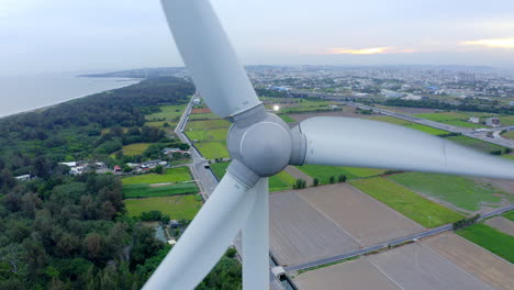 Primer-Plano-De-La-Turbina-Eólica-Terrestre-Girando-Frente-A-Los-Campos-De-Plantación-Y-La-Costa-En-China---Vuelo-Aéreo-Hacia-Atrás