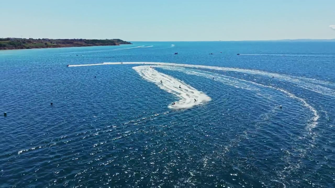Una gara di jet ski si svolge in una giornata di sole in un mare limpido e azzurro con più piloti che sfrecciano sull'acqua.
