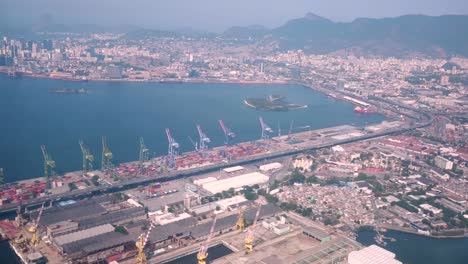 volando sobre la zona portuaria de río de janeiro con sus áreas de maquinaria y stock y al fondo el centro de la ciudad con monumentos famosos reconocibles