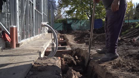 Construction-worker-digs-trench-in-ground-with-shovel