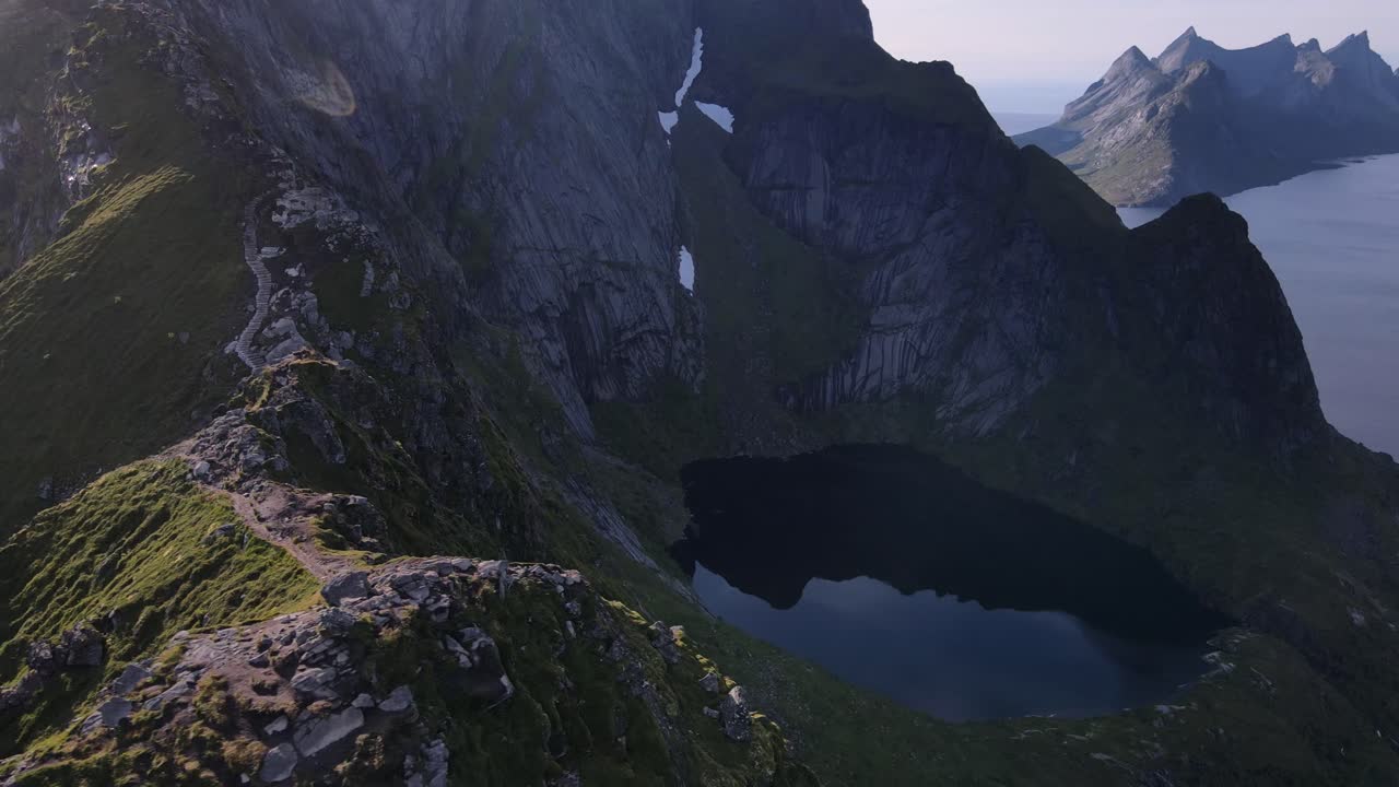 vuelo aéreo a lo largo de la escarpada cordillera montañosa reinebringen con senderos para caminatas que revelan fiordos y cumbres rocosas de las islas lofoten