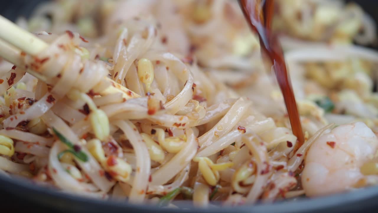 Gros plan sur des nouilles Pad Thai mélangées avec des flocons de piment