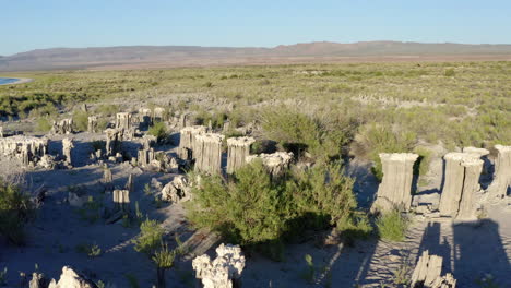 Aerial-view-of-unique-tufa-rock-formations-at-Mono-Lake,-highlighting-the-distinct-columns-and-the-surrounding-desert-vegetation-under-a-clear-blue-sky