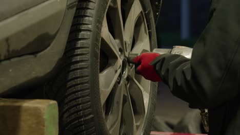 close-up of mechanic's hands with red gloves screwing a wheel with automatic screwdriver