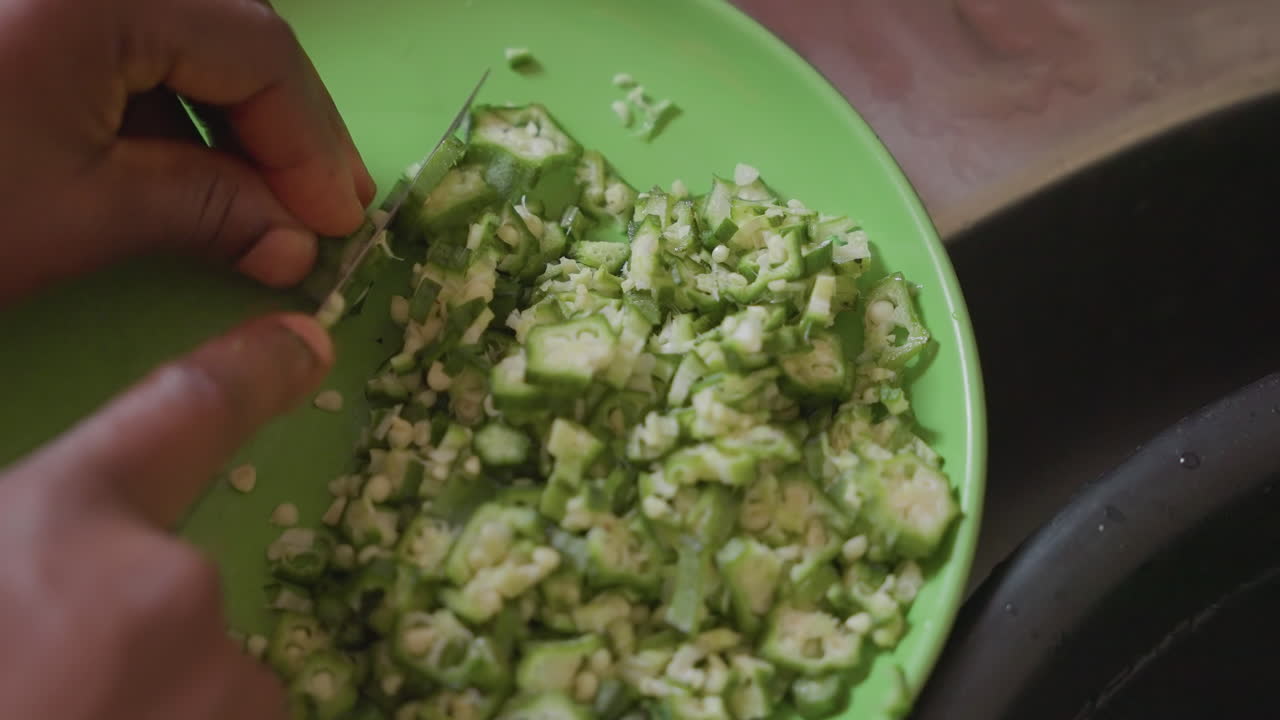 Mørke hænder blander hakket grøn salat nær vask, gadesælger eller markedskok trimmer og kaster grøntsager med kniv, nærbillede af rytmisk bevægelse, tekstureret skål, bylys og taktil madoplevelse.