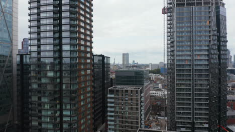 Descending-footage-on-tall-modern-buildings-with-glossy-glass-facades-reflecting-sky.-Office-or-apartment-downtown-buildings.-London,-UK