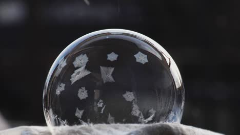 una burbuja de jabón se encuentra en la nieve sobre un fondo negro, los copos de nieve caen sobre ella y se congelan. patrón de globo de hielo