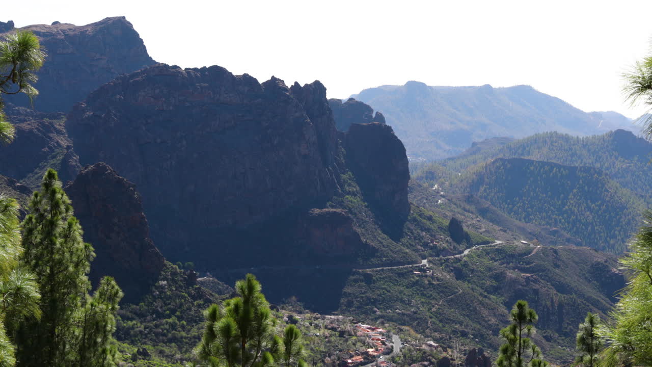The narrow forest, winding road leading under a ridge of rocks spinning in a national park with passage of cars during sunny days Gran Canary island 4k slow motion capture at 60fps