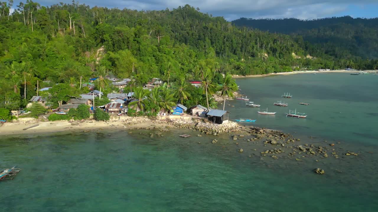 Comunità di pescatori che vive in semplici abitazioni lungo una spiaggia tropicale sabbiosa, circondata da vegetazione lussureggiante e palme. Time lapse con rampa di velocità. Vista aerea unica, panorama orbitale ampio con vista dall'alto da drone.