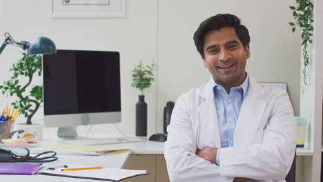 portrait of smiling male doctor wearing white coat sitting at desk in office