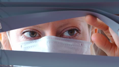 woman wearing a mask looking through blinds