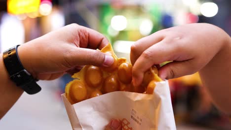 hands sharing bubble waffles on a busy street