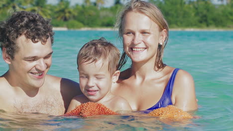 Los-Padres-Y-Su-Pequeño-Hijo-En-Agua-De-Mar-Sosteniendo-Estrellas-De-Mar.