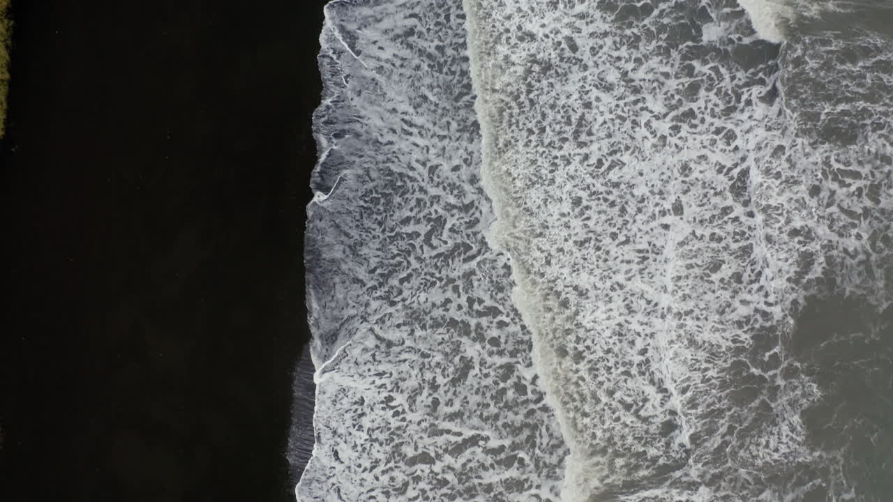 Aerial: Top down aerial view of waves breaking on volcanic black sand beach