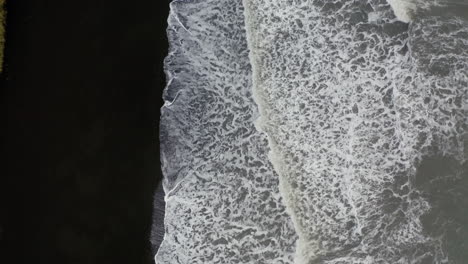 aerial: top down aerial view of waves breaking on volcanic black sand beach