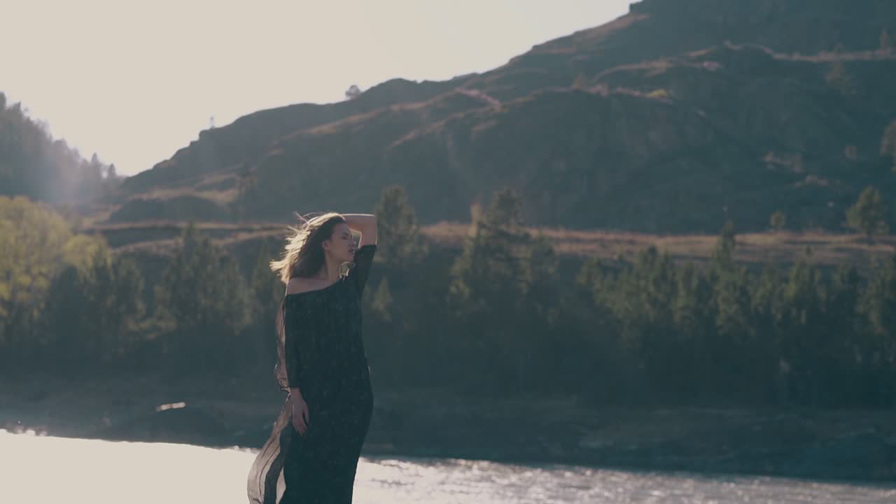 pretty girl in stylish dress stands against mountain river