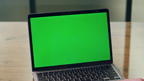 una mujer usando una computadora portátil de pantalla verde en una oficina de primer plano. una mujer de negocios anónima trabajando.
