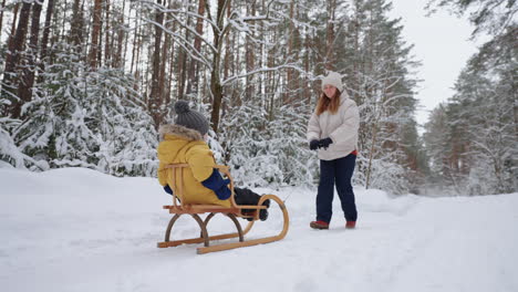 Junge-Mutter-Und-Kleiner-Sohn-Fahren-Schlitten-Im-Winterwald-Und-Wandern-Zwischen-Hohen,-Schneebedeckten-Fichten