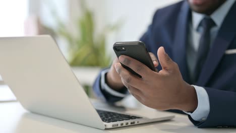 african businessman with laptop using smartphone, close up