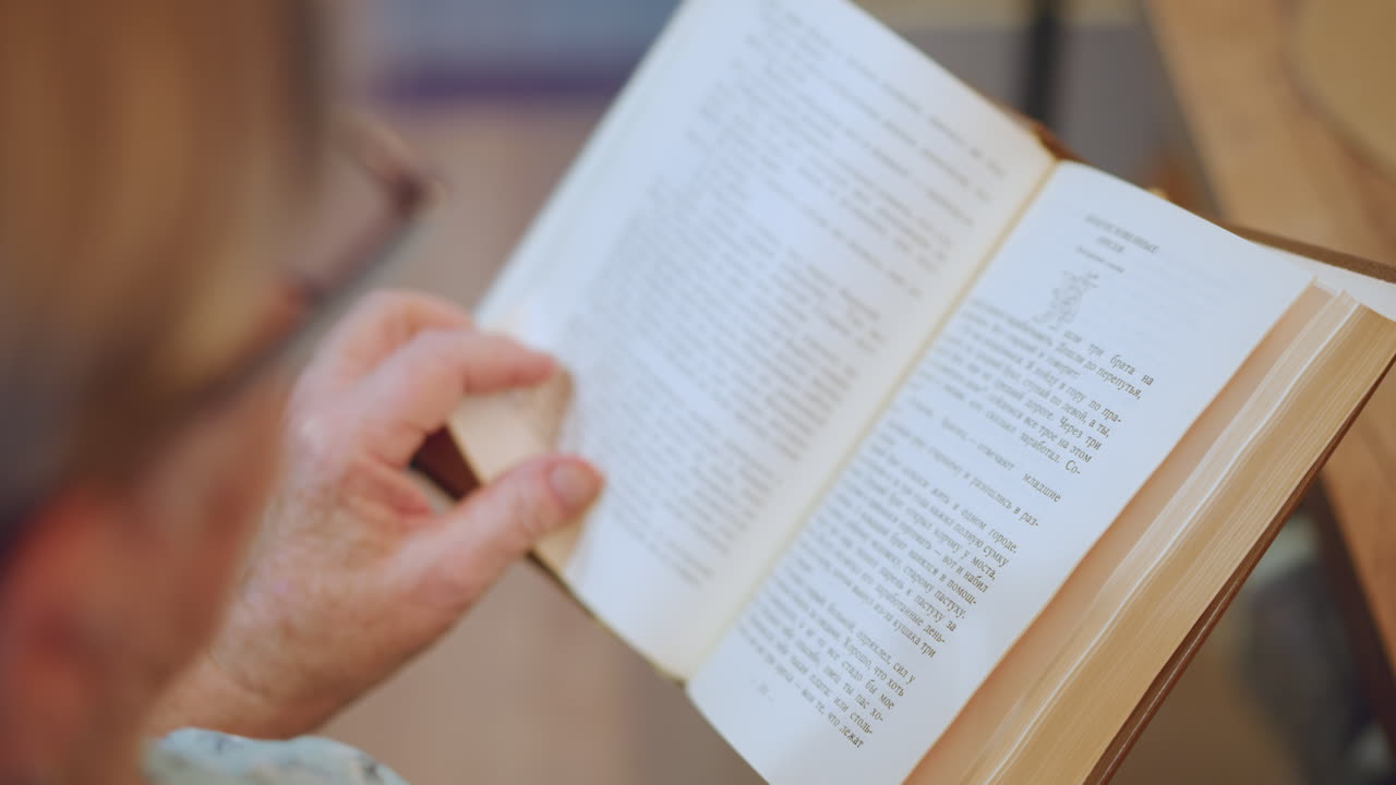 Grandmother studies book calmly. Grandmother wearing glasses carefully reviewing her book peacefully. An elderly woman with spectacles thoroughly examining her open book in tranquil environment