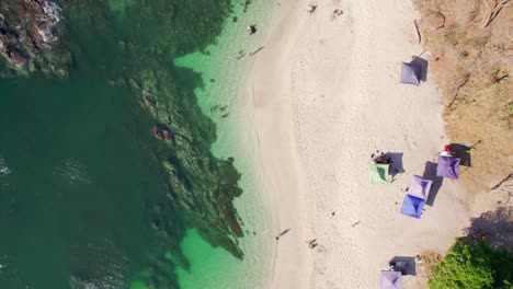 Eine-Drohne-Von-Oben-Nach-Unten-Senkt-Aufnahmen-Von-Sonnenschirmen-Am-Strand-Neben-Dem-Klaren-Meer