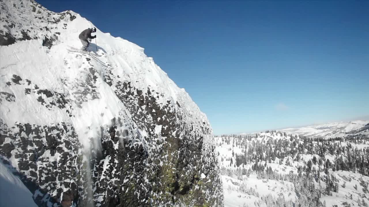 스키어가 산에서 뛰어내리고 다른 사람이 아래에 앉는다.