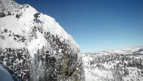 a skier jumps off the side of a mountain and another person sits below