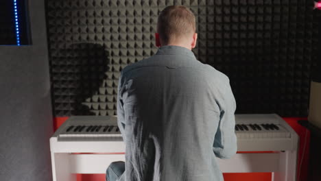 back shot of a man in a blue shirt playing a white piano, with his shadow cast on a black acoustic wall. the scene captures the contrast and texture in a music studio setting