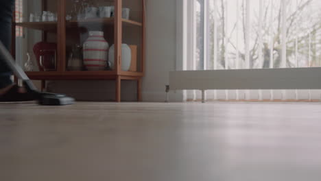 young male cleaning the house with a vacuum cleaner cleaning the wooden floor zoom in detail