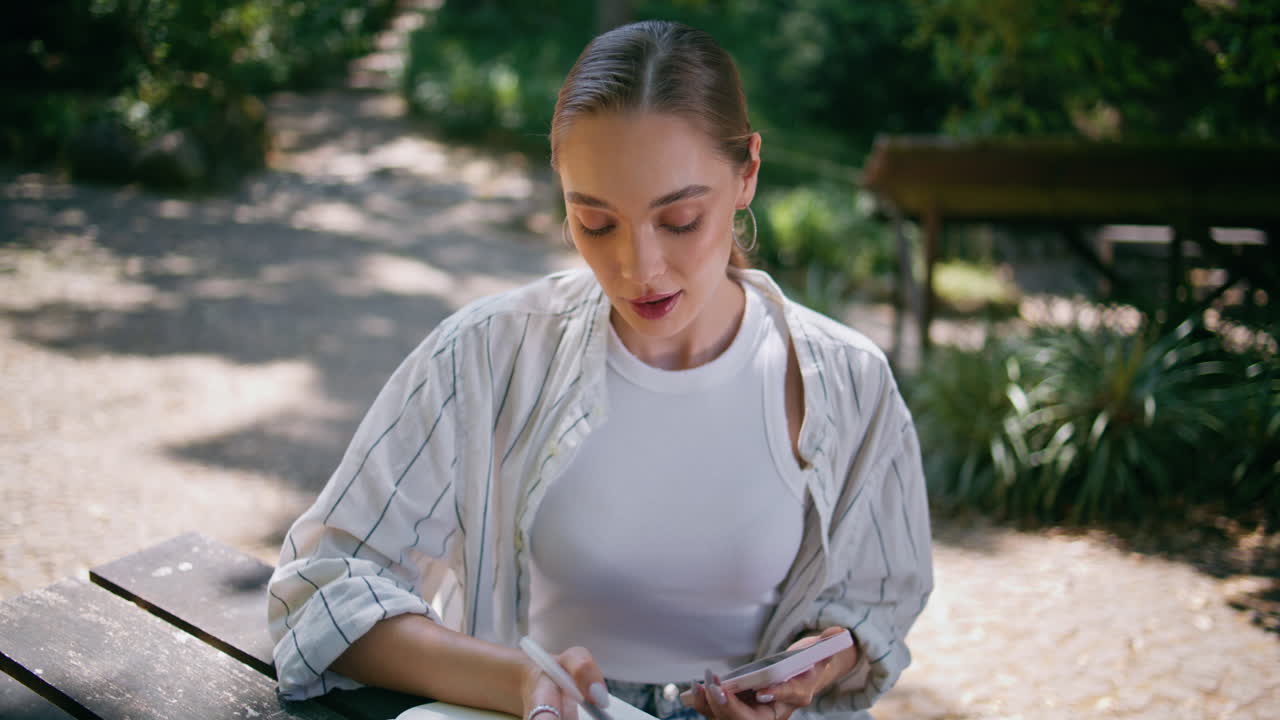 chica relajada desplazando el teléfono inteligente buscando información en la mesa del parque de cerca.