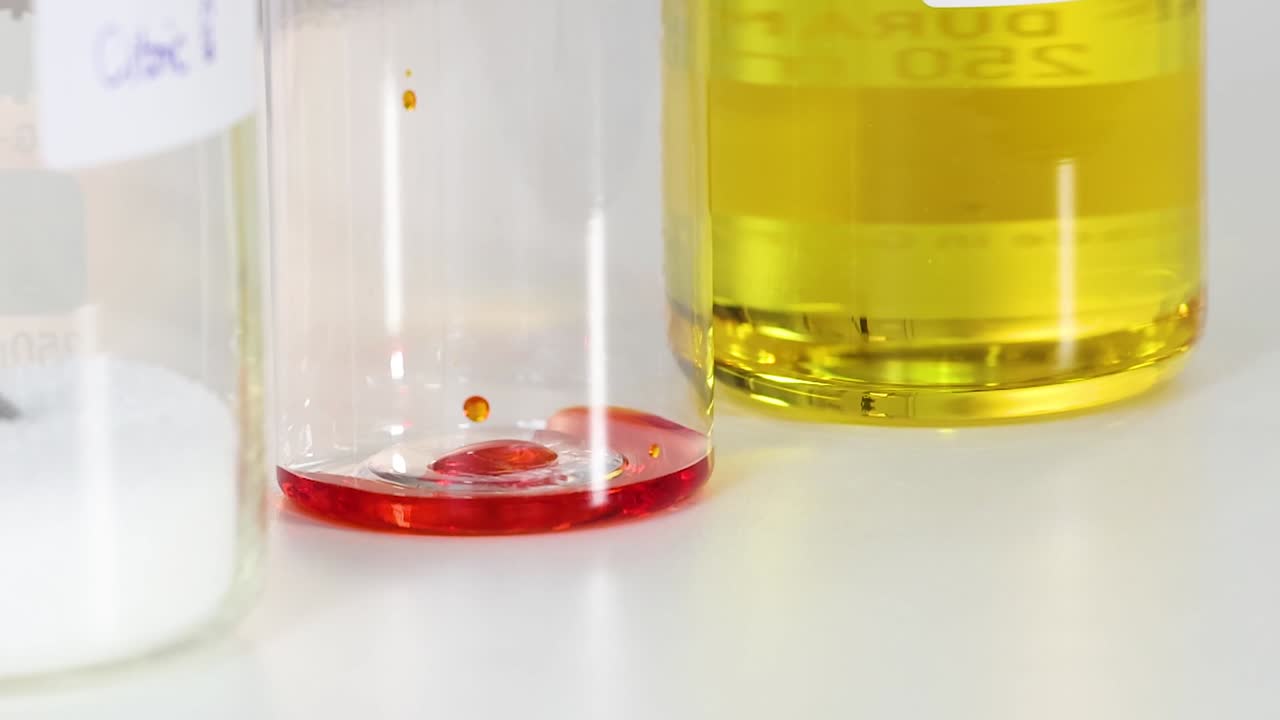 Observe red droplets interacting with yellow liquid in a clear container, showcasing fluid dynamics and color contrast.