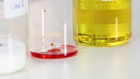 observe red droplets interacting with yellow liquid in a clear container, showcasing fluid dynamics and color contrast.