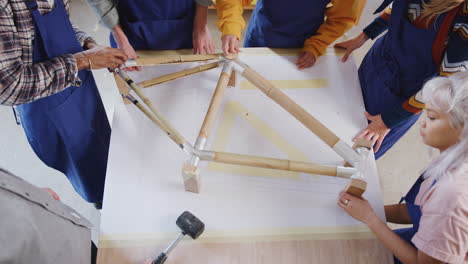 Overhead Shot Of Multi-Cultural Team In Workshop Assembling Sustainable Bamboo Bicycle Frame
