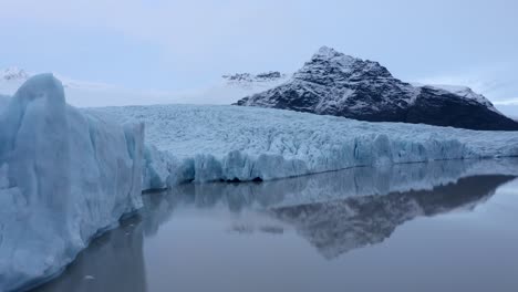 Aerial-flyover-Fjallsárlón-glacier-lagoon-in-South-Iceland-during-cloudy-day---Tranquil-water-with-iced-shoreline-in-Nature