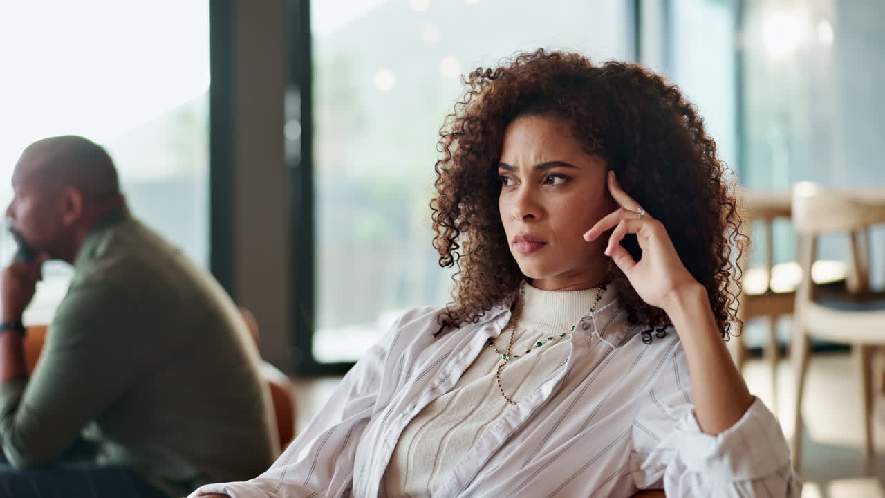 A woman with curly hair is sitting indoors looking pensive