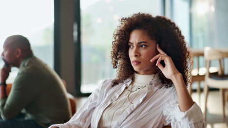a woman with curly hair is sitting indoors looking pensive