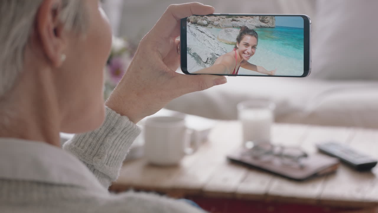 mujer madura que tiene una videochat usando un teléfono inteligente saludando a su hija en una playa de vacaciones en italia compartiendo experiencia de viaje en el teléfono móvil disfrutando de la conexión hablando con la abuela 4k