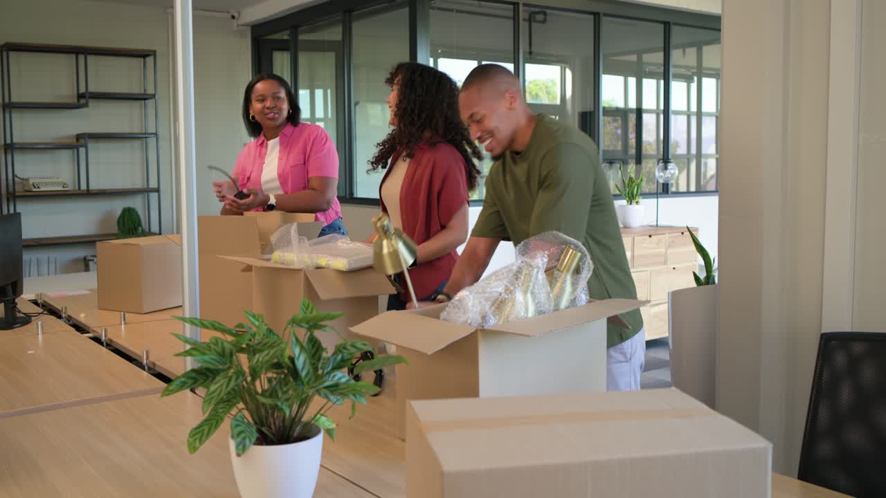 African American team in jackets entering office with boxes, unpacking lamp and arranging workspace