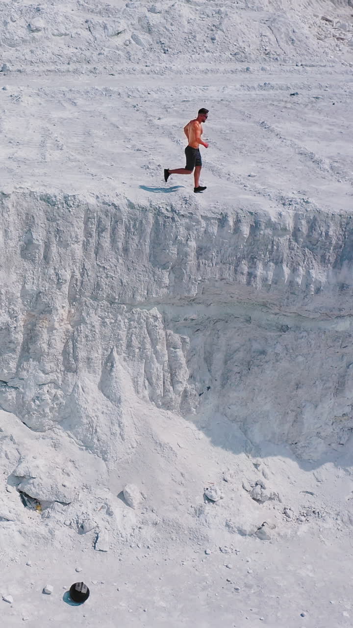 Sportsman on a white canyon. Healthy man in shorts doing his daily training outdoors. Strong athlete runs on the rocky hill in a sunny summer day. Aerial view. Vertical video