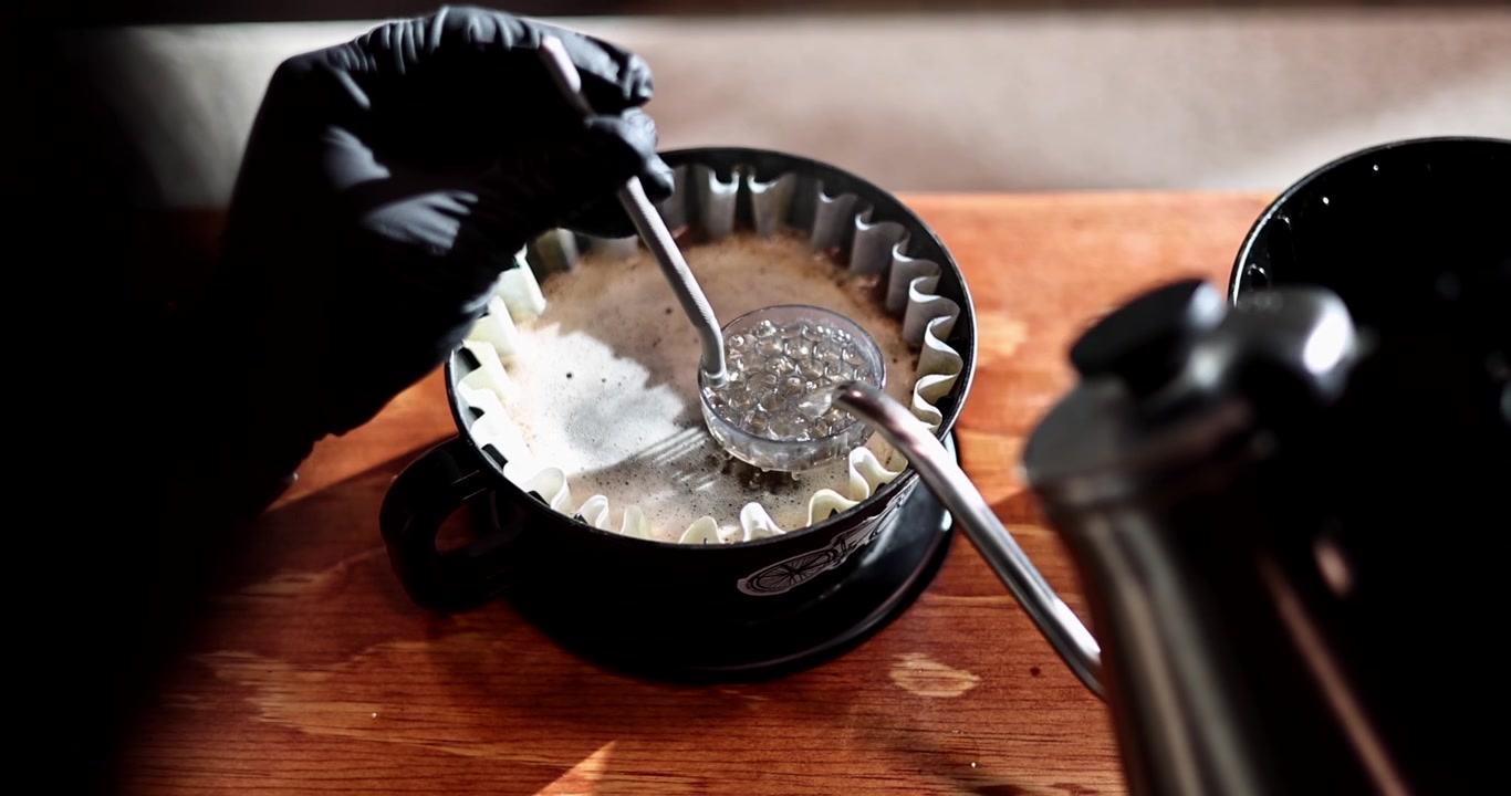 Manuell pour over kaffeekstraksjon oppnår jevn metning mens "bloom" legger seg i papirfilteret, oversikt i sakte film.