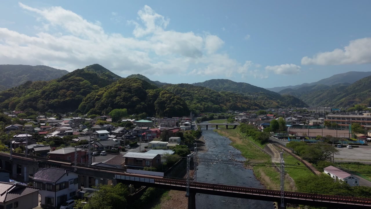 Cittadina nella valle del fiume attraversata da un viadotto ferroviario sopraelevato, montagne boscose a Kawazu, Izu, Giappone, in un pomeriggio luminoso, ripresa aerea con drone
