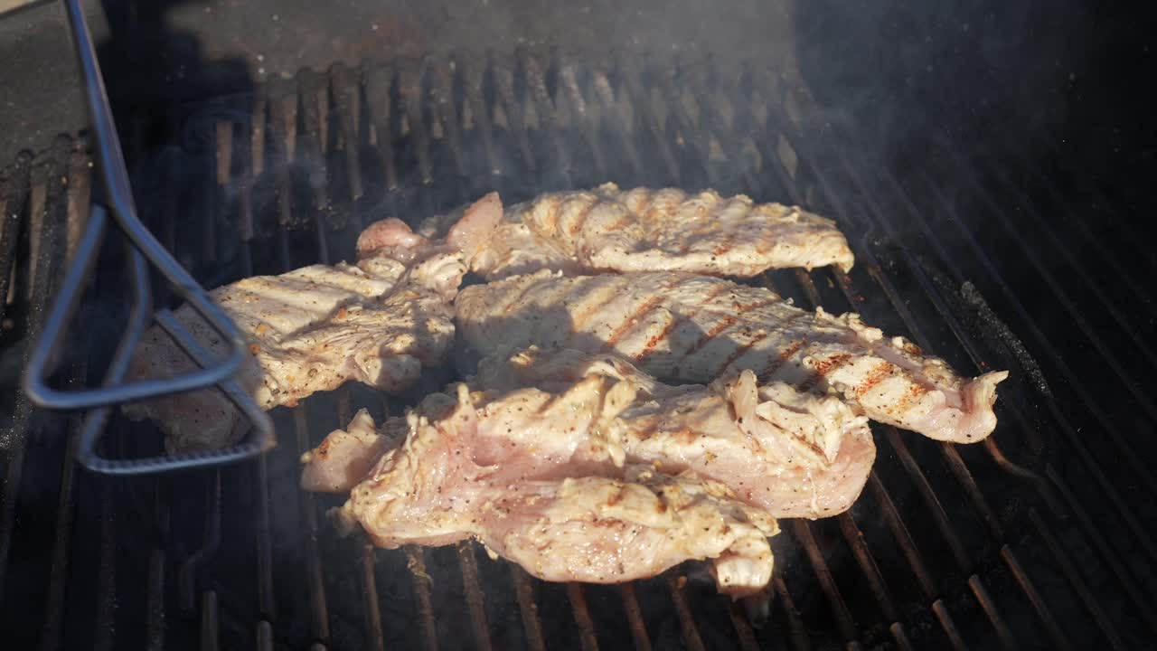 volteando pechugas de pollo orgánicas en la parrilla de la barbacoa con pinzas - cámara lenta aislada