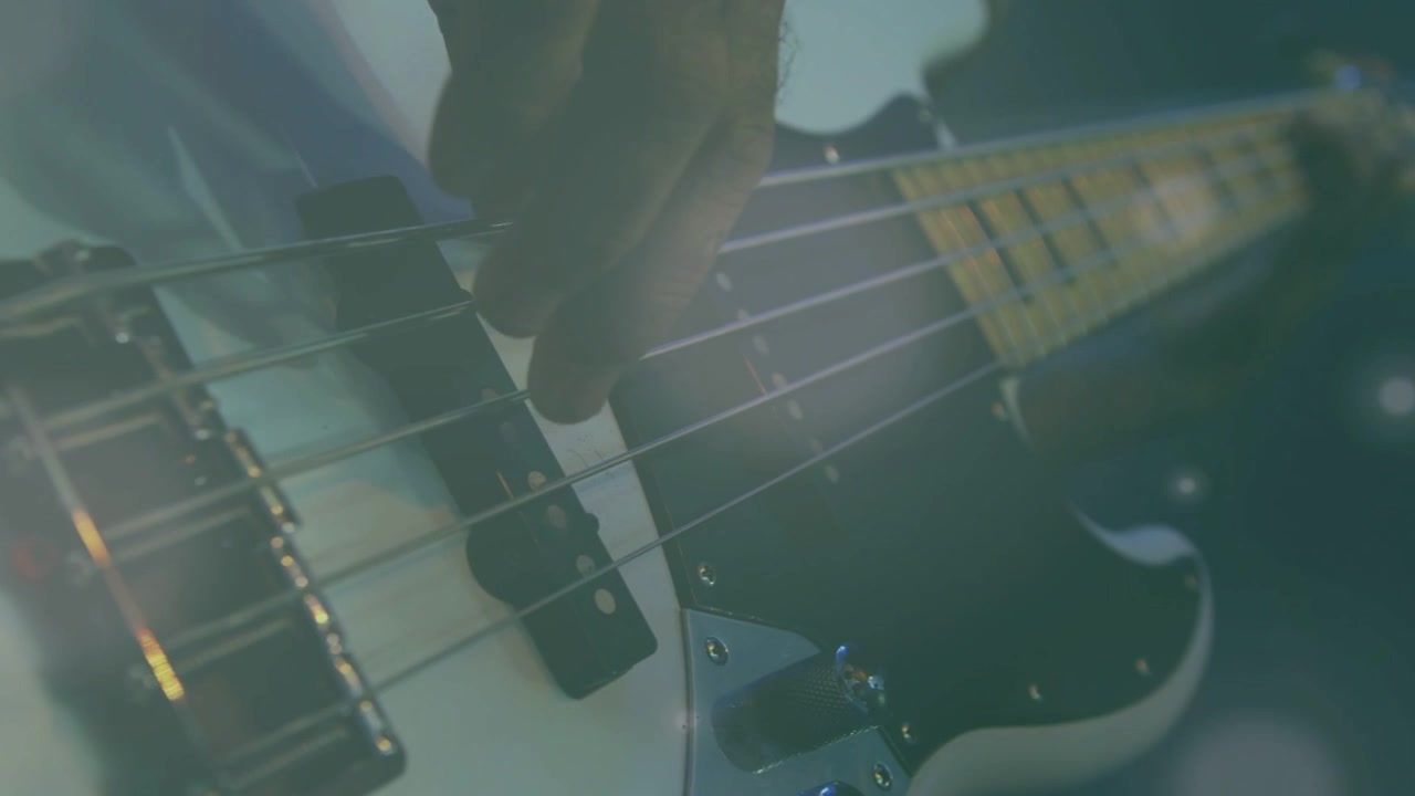 Mano destra del bassista che sfiora i pickup, iniziando a pizzicare e far rotolare le corde, creando musica incalzante con effetto bokeh