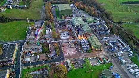 rotating overhead aerial footage of a large industrial plant showing pipework structures, buildings, cooling towers, steam, and work vehicles