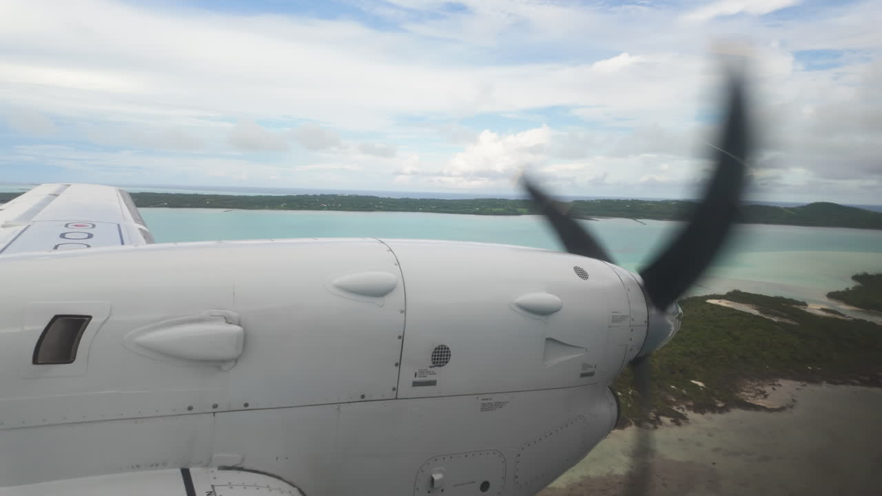 Clear slow motion view from inside airplane looking out at wing and propellor over tropical islands