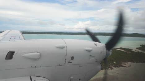 clear slow motion view from inside airplane looking out at wing and propellor over tropical islands