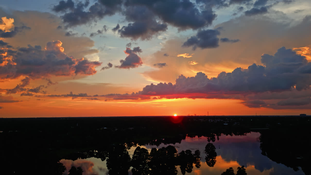 Breathtaking evening sunset reflecting on still lake, soft orange and pink tones create tranquil backdrop as sun dips below horizon, aerial slowly flying forward